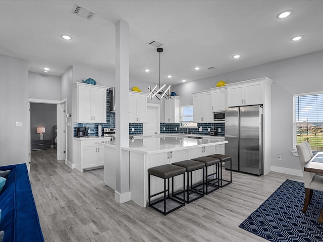 kitchen with an inviting chandelier, a kitchen island, backsplash, light countertops, and appliances with stainless steel finishes