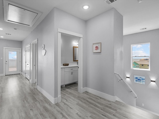 hallway with baseboards, light wood-type flooring, an upstairs landing, and visible vents
