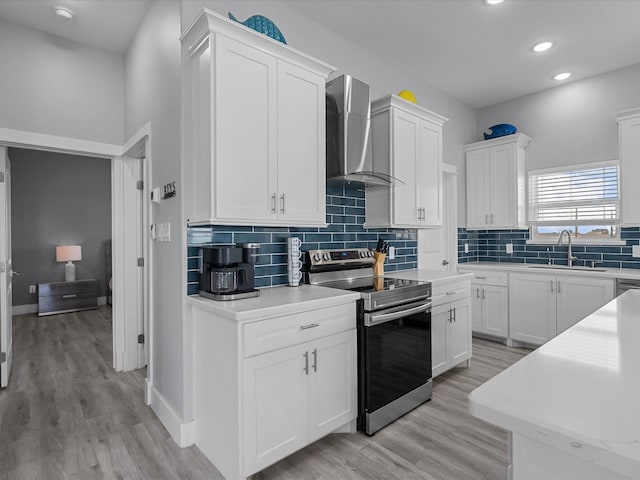 kitchen with a sink, wall chimney exhaust hood, white cabinets, and electric stove