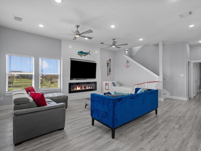 living room featuring light wood-type flooring, ceiling fan, and a fireplace