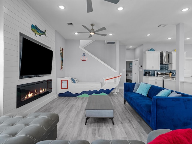 living room with a fireplace, ceiling fan, and light hardwood / wood-style flooring