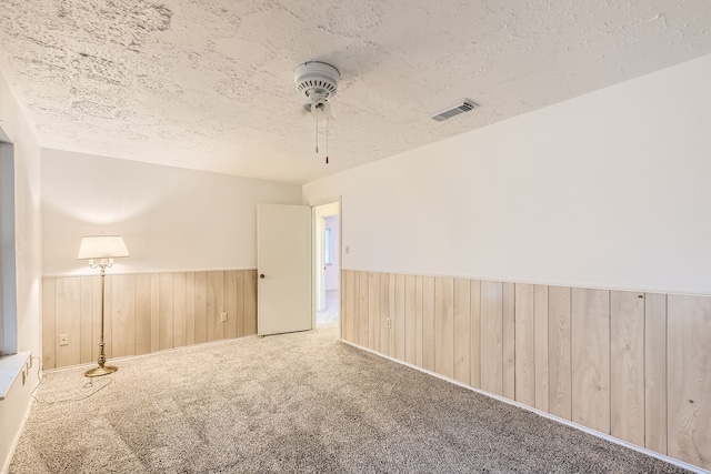 spare room with ceiling fan, wooden walls, carpet, and a textured ceiling