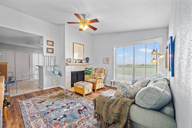 living room featuring wood finished floors, baseboards, a fireplace, ceiling fan, and a textured ceiling