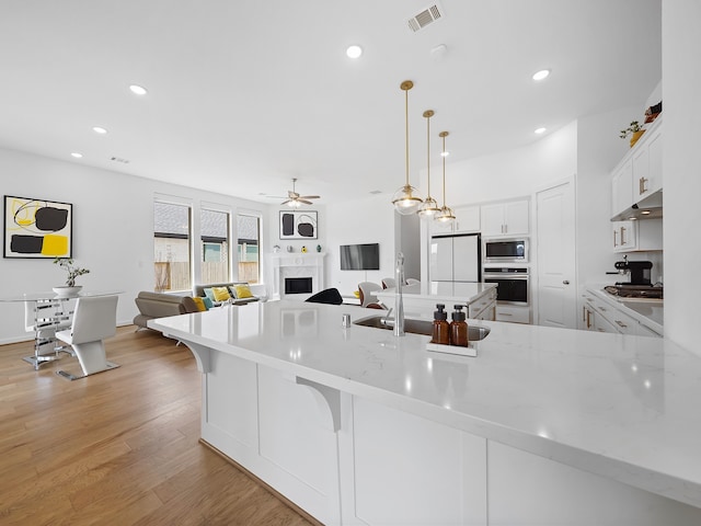 kitchen featuring stainless steel appliances, a premium fireplace, ceiling fan, hanging light fixtures, and white cabinets