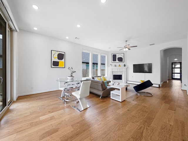 living room with a baseboard heating unit, a premium fireplace, ceiling fan, and light wood-type flooring