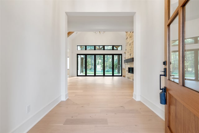 foyer featuring a chandelier, a towering ceiling, light hardwood / wood-style floors, and a stone fireplace