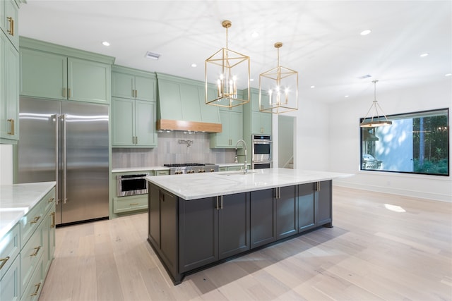 kitchen with appliances with stainless steel finishes, light stone counters, hanging light fixtures, and an island with sink