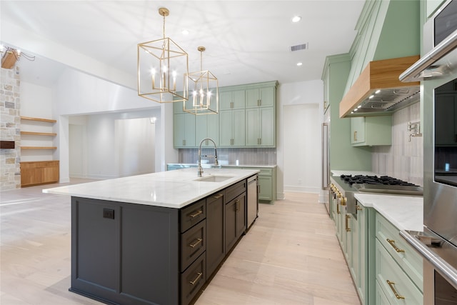 kitchen with appliances with stainless steel finishes, tasteful backsplash, light stone counters, decorative light fixtures, and a center island with sink