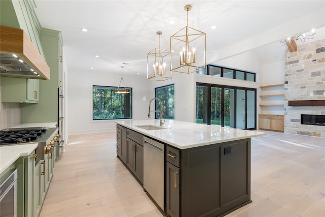 kitchen featuring sink, hanging light fixtures, a stone fireplace, an island with sink, and custom exhaust hood