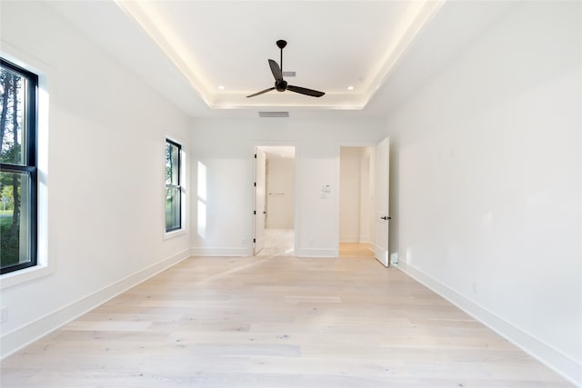 unfurnished bedroom with ceiling fan, a raised ceiling, and light wood-type flooring