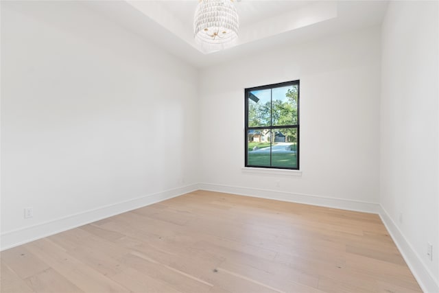 spare room featuring a raised ceiling, light wood-type flooring, and a notable chandelier