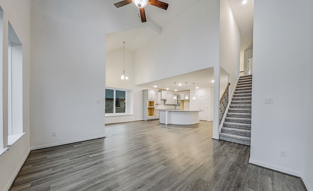 unfurnished living room with high vaulted ceiling, dark wood-type flooring, and ceiling fan with notable chandelier