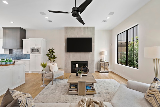 living room featuring ceiling fan, a fireplace, and light hardwood / wood-style floors