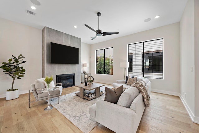 living room featuring light hardwood / wood-style flooring, ceiling fan, and a fireplace