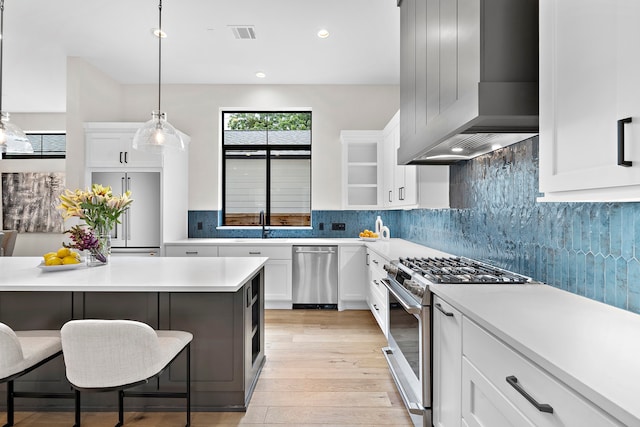 kitchen featuring light wood-type flooring, stainless steel appliances, wall chimney exhaust hood, a breakfast bar area, and white cabinets