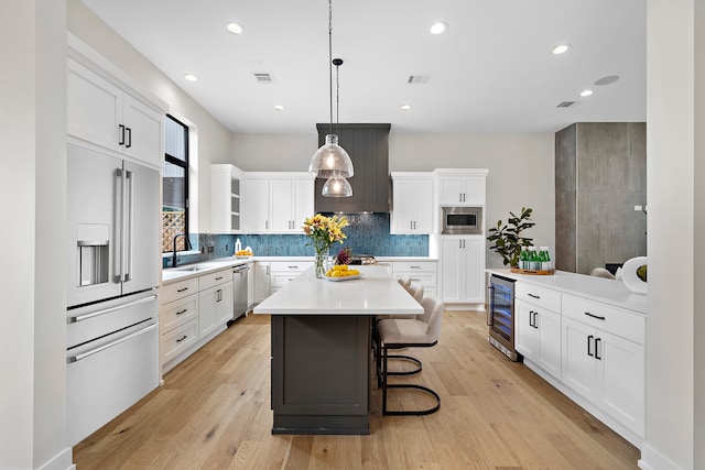 kitchen featuring built in appliances, beverage cooler, a kitchen island, hanging light fixtures, and white cabinets