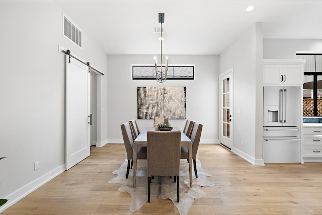 dining space featuring a barn door, light wood-type flooring, and a chandelier