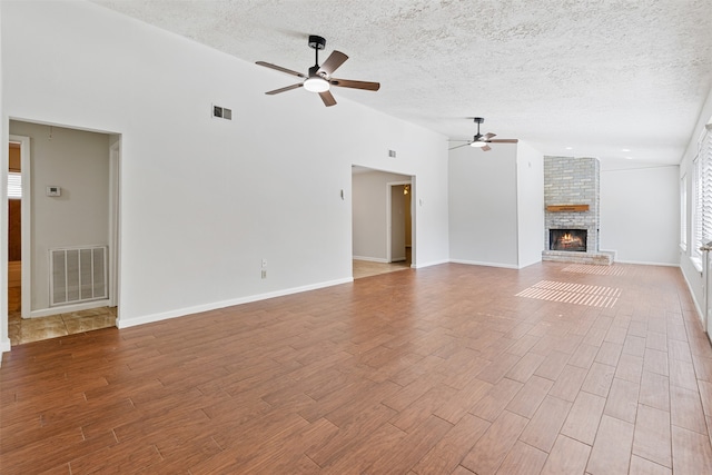 unfurnished living room with a textured ceiling, ceiling fan, a brick fireplace, and hardwood / wood-style flooring