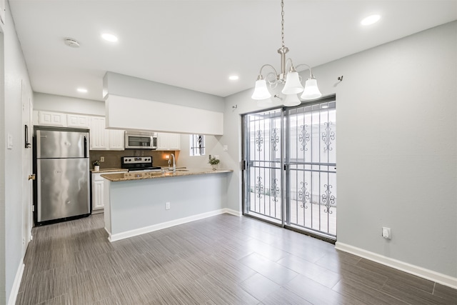 kitchen with an inviting chandelier, kitchen peninsula, appliances with stainless steel finishes, hanging light fixtures, and white cabinets