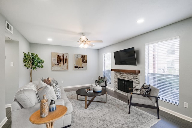 living room with ceiling fan, a stone fireplace, and hardwood / wood-style flooring