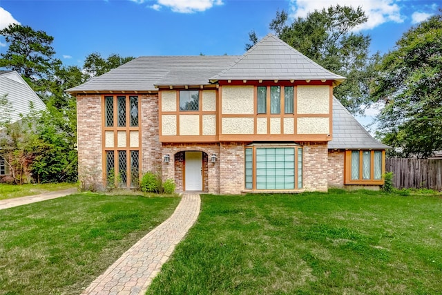 tudor-style house with brick siding, a front yard, and fence