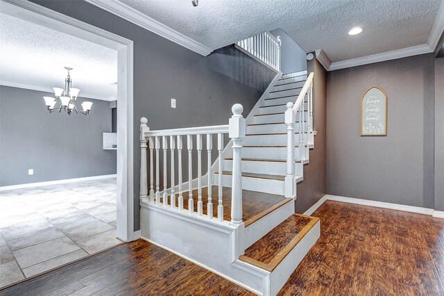 staircase with a textured ceiling, ornamental molding, hardwood / wood-style floors, and an inviting chandelier