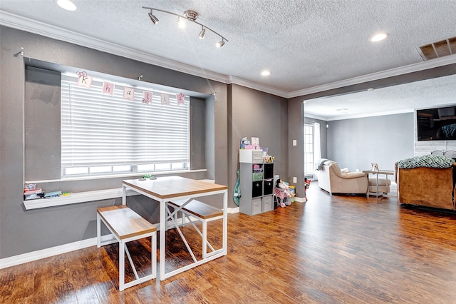 dining area featuring a textured ceiling, rail lighting, ornamental molding, and hardwood / wood-style floors