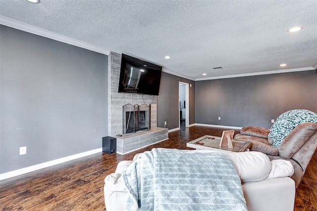 living room featuring dark wood-type flooring, a tile fireplace, crown molding, and a textured ceiling