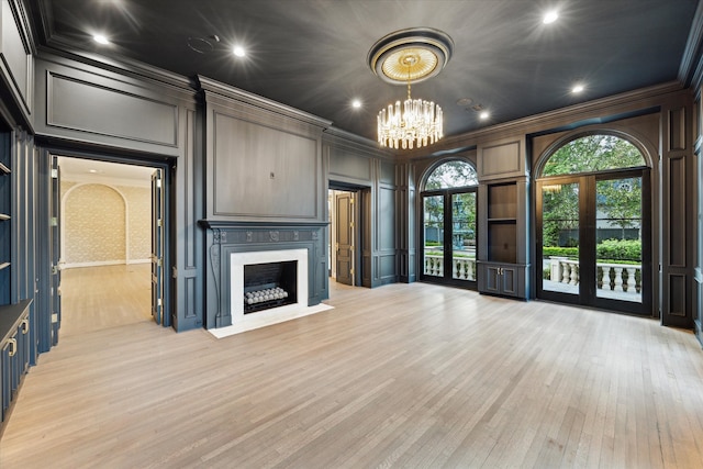 unfurnished living room featuring a fireplace, a notable chandelier, french doors, ornamental molding, and light wood-type flooring