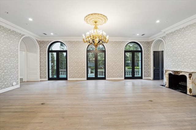 unfurnished living room with crown molding, french doors, light hardwood / wood-style flooring, and a notable chandelier