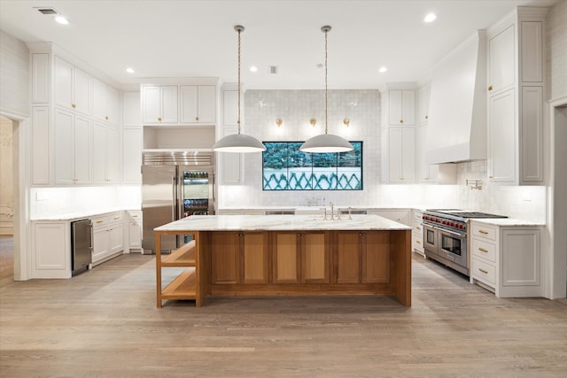 kitchen featuring a large island with sink, high end appliances, light stone countertops, and white cabinetry