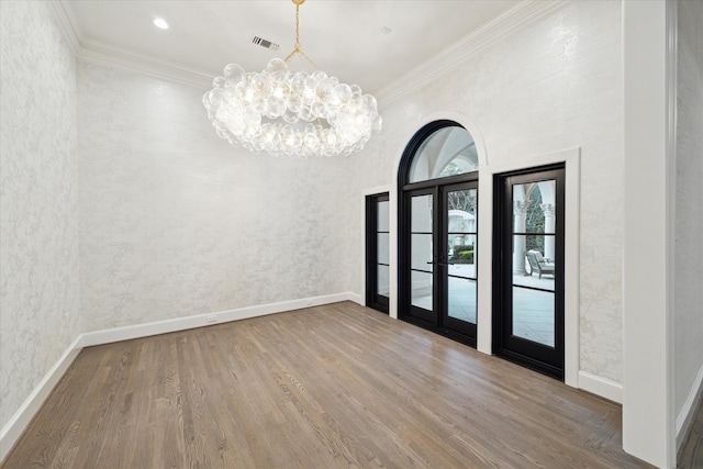 spare room featuring french doors, ornamental molding, hardwood / wood-style floors, and a chandelier