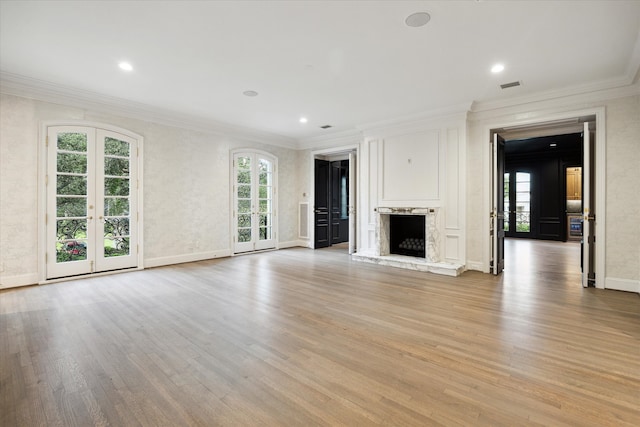 unfurnished living room with ornamental molding, a high end fireplace, light wood-type flooring, and french doors