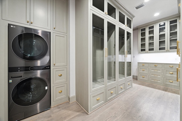 laundry room featuring cabinets, light hardwood / wood-style flooring, and stacked washer and dryer