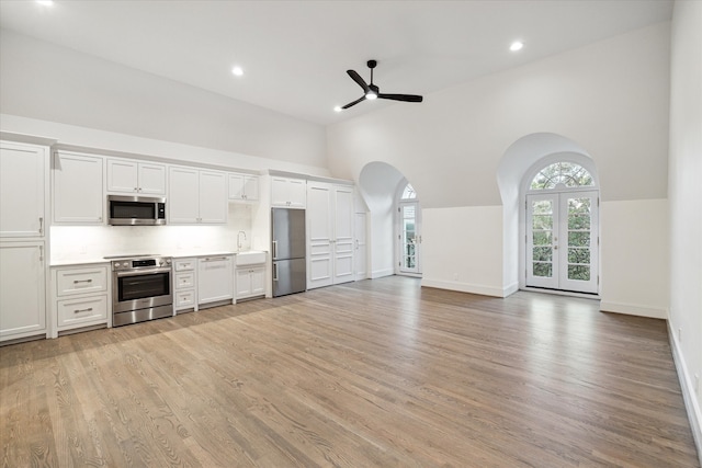 kitchen with a high ceiling, white cabinetry, light hardwood / wood-style flooring, stainless steel appliances, and ceiling fan