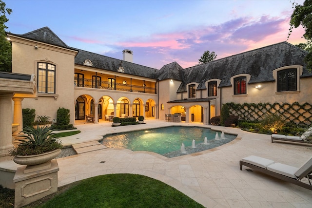 pool at dusk with a patio area and pool water feature