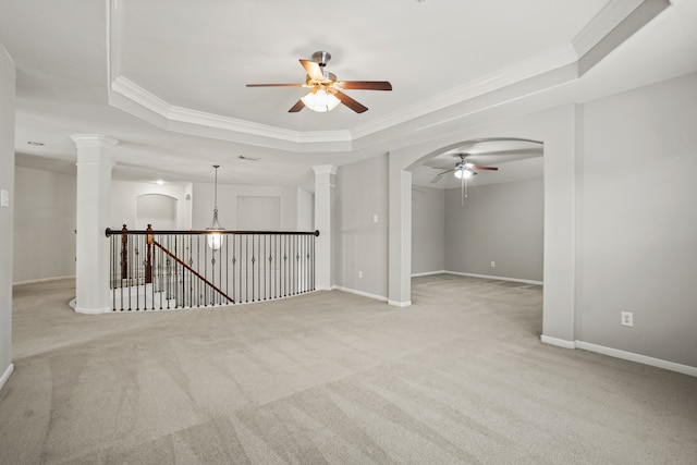 empty room featuring decorative columns, light colored carpet, a tray ceiling, and ceiling fan