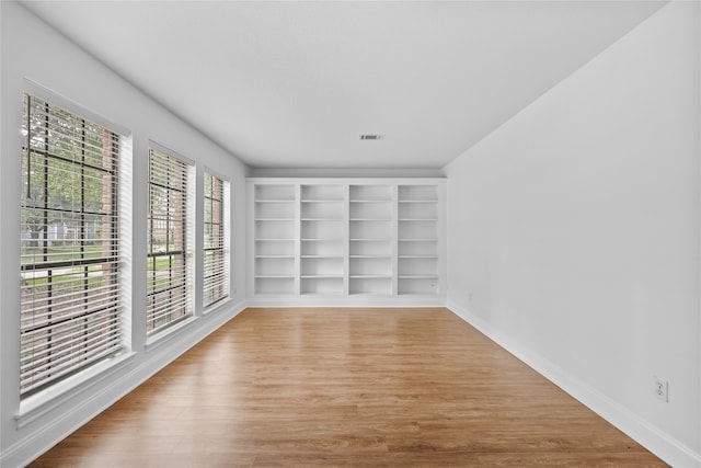 unfurnished room featuring built in features and hardwood / wood-style flooring