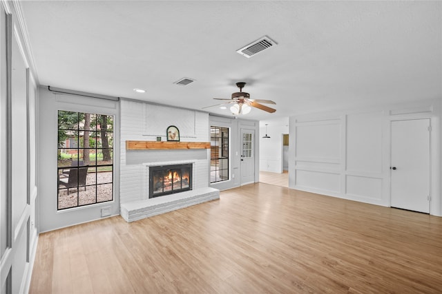 unfurnished living room with ceiling fan, light hardwood / wood-style floors, a textured ceiling, and a brick fireplace