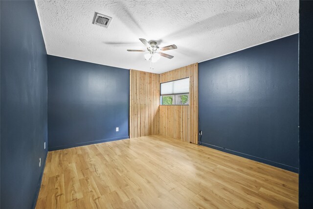 empty room with a textured ceiling, hardwood / wood-style flooring, wood walls, and ceiling fan