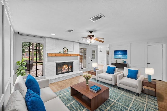 living room with a textured ceiling, wood-type flooring, ceiling fan, and a brick fireplace