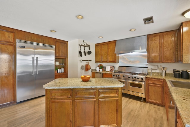 kitchen featuring light wood-type flooring, wall chimney exhaust hood, a center island, and premium appliances