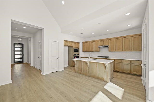 kitchen with a kitchen island with sink, stainless steel appliances, high vaulted ceiling, light hardwood / wood-style floors, and decorative backsplash