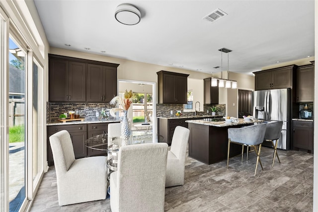 kitchen with stainless steel fridge with ice dispenser, sink, hardwood / wood-style floors, a kitchen island, and hanging light fixtures