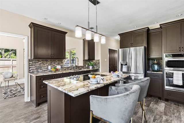 kitchen featuring dark brown cabinetry, light stone counters, pendant lighting, a kitchen island, and appliances with stainless steel finishes