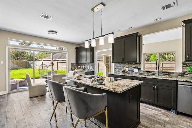 kitchen featuring pendant lighting, black electric stovetop, stainless steel dishwasher, a kitchen island, and light stone counters