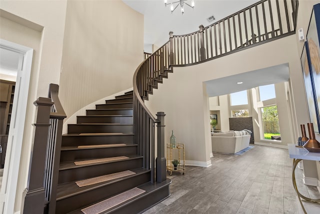 stairs featuring hardwood / wood-style floors, a towering ceiling, and an inviting chandelier