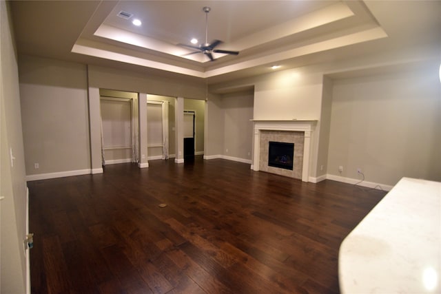 unfurnished living room with a raised ceiling, a fireplace, dark hardwood / wood-style flooring, and ceiling fan