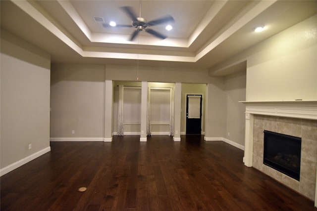 unfurnished living room featuring ceiling fan, a raised ceiling, a tiled fireplace, and dark hardwood / wood-style floors