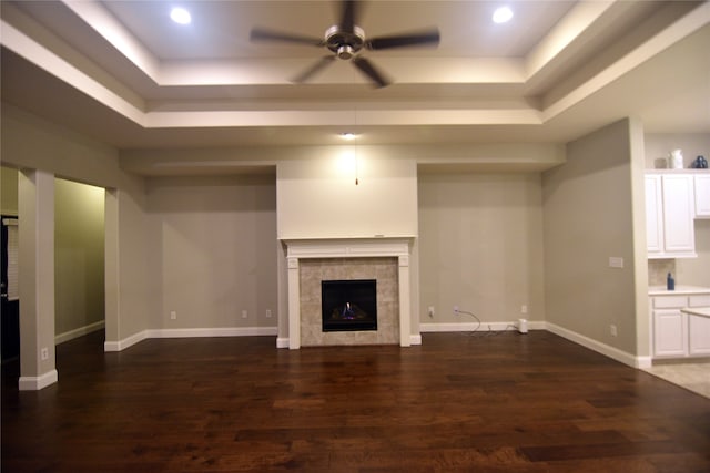 unfurnished living room featuring ceiling fan, a fireplace, a raised ceiling, and dark wood-type flooring